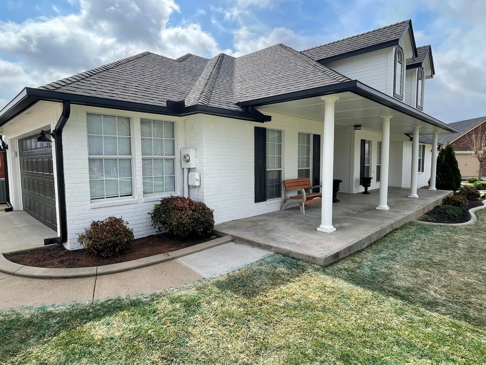 A white brick house with a porch and a gray roof.