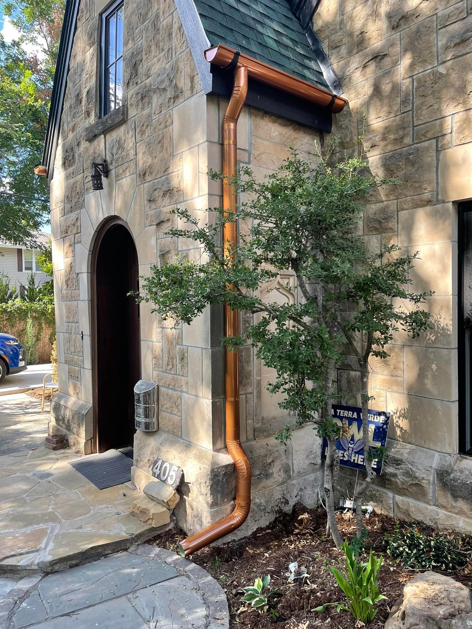A copper gutter is installed on the side of a stone building.