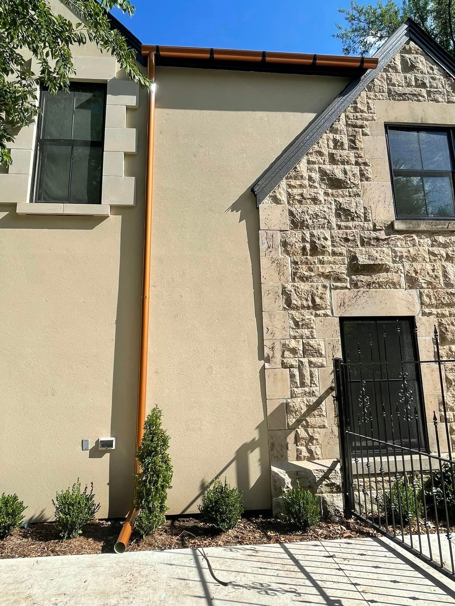 A large stone house with a copper gutter on the side of it.