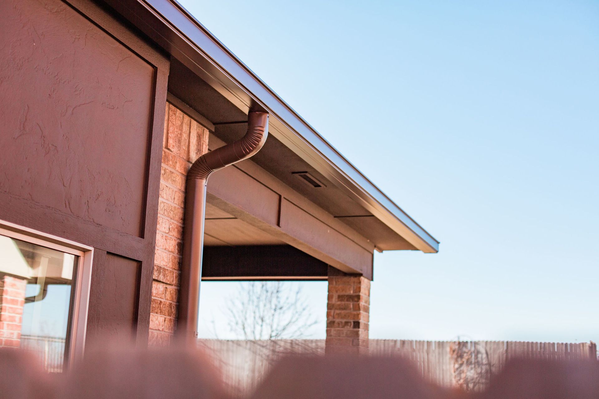 A house with a gutter on the side of it and a fence in the background.