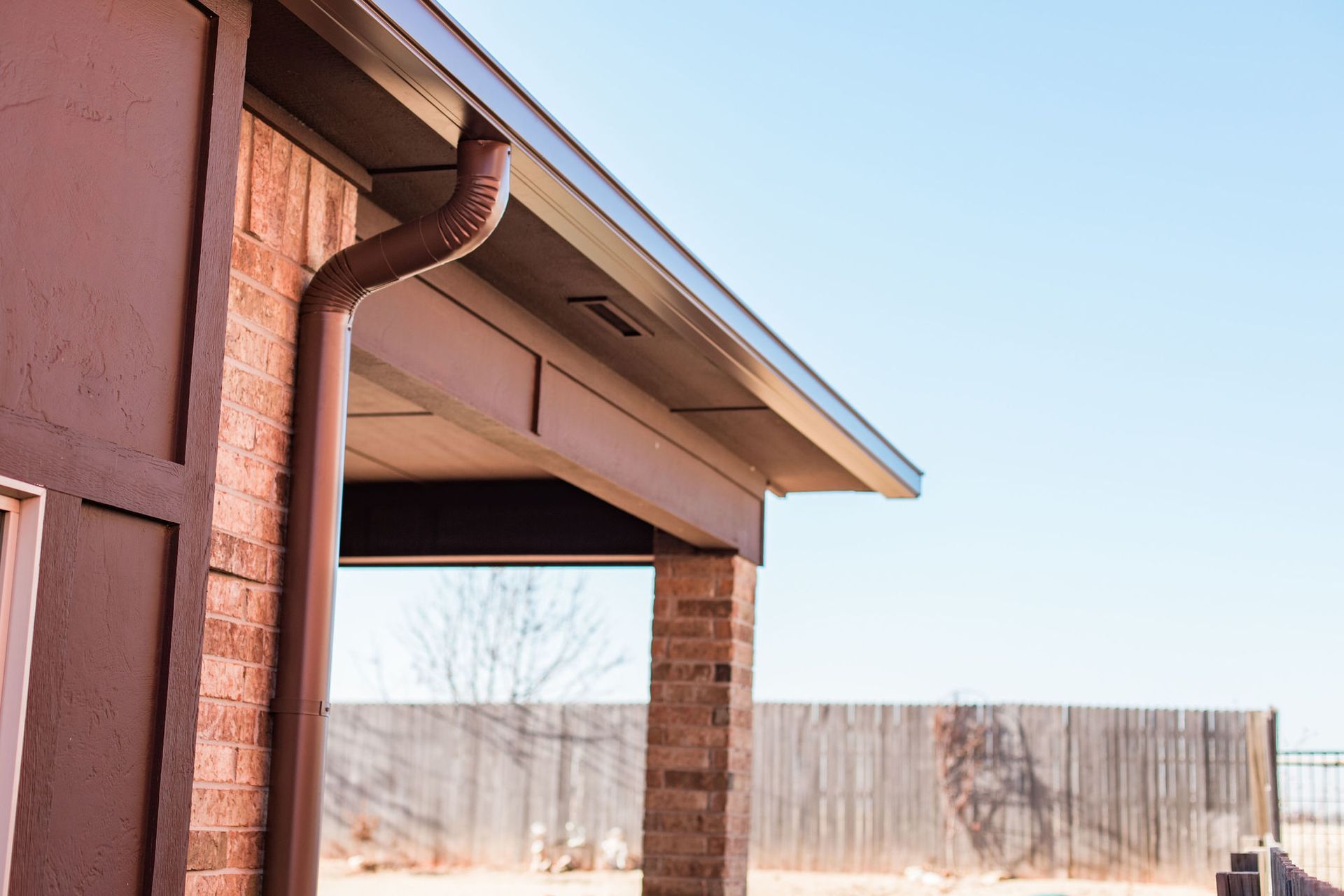 A house with a gutter on the side of it and a fence in the background.