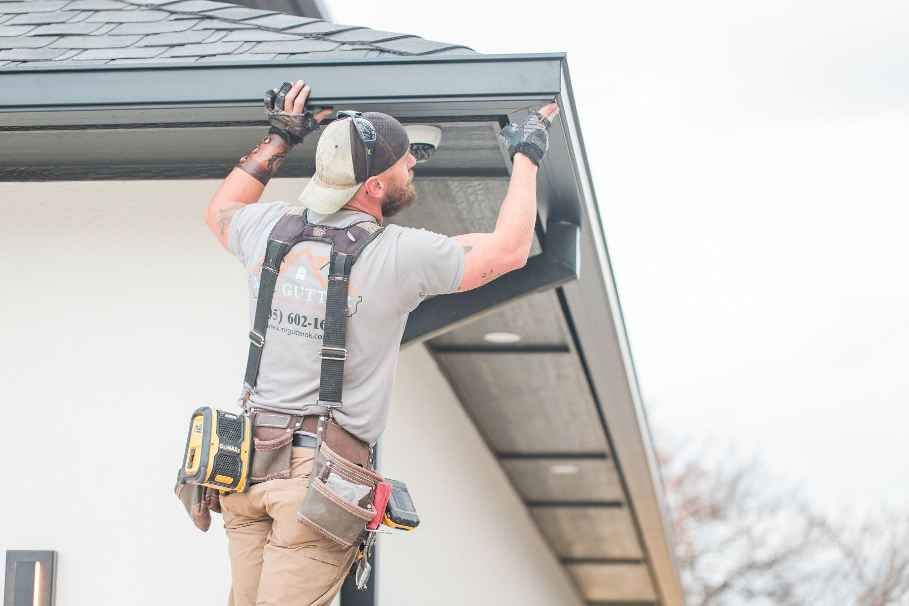A man is working on a gutter on the side of a house.
