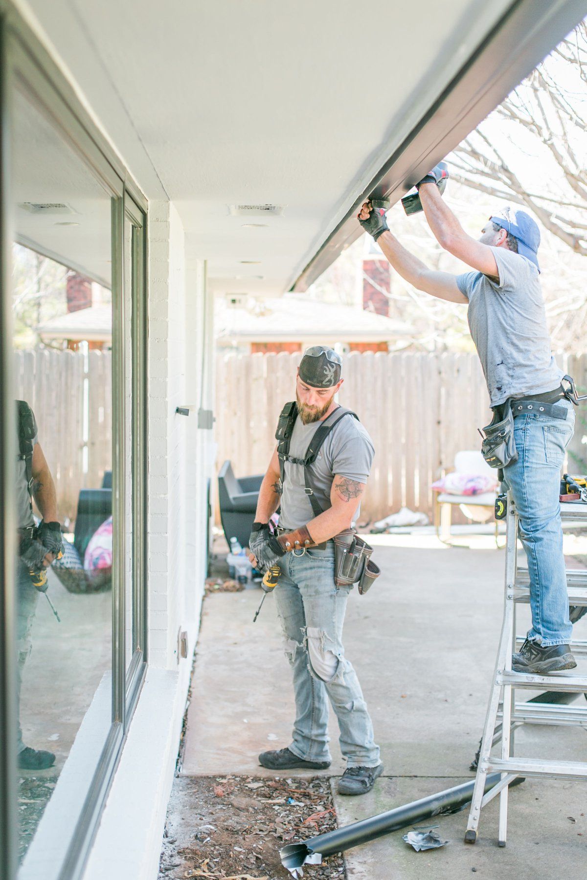 Two men are working on a gutter on the side of a house.