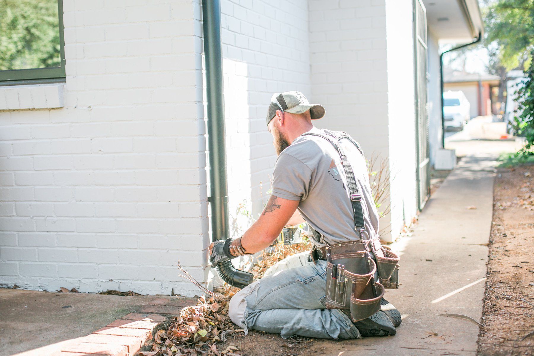 A man is kneeling down in front of a white brick building.