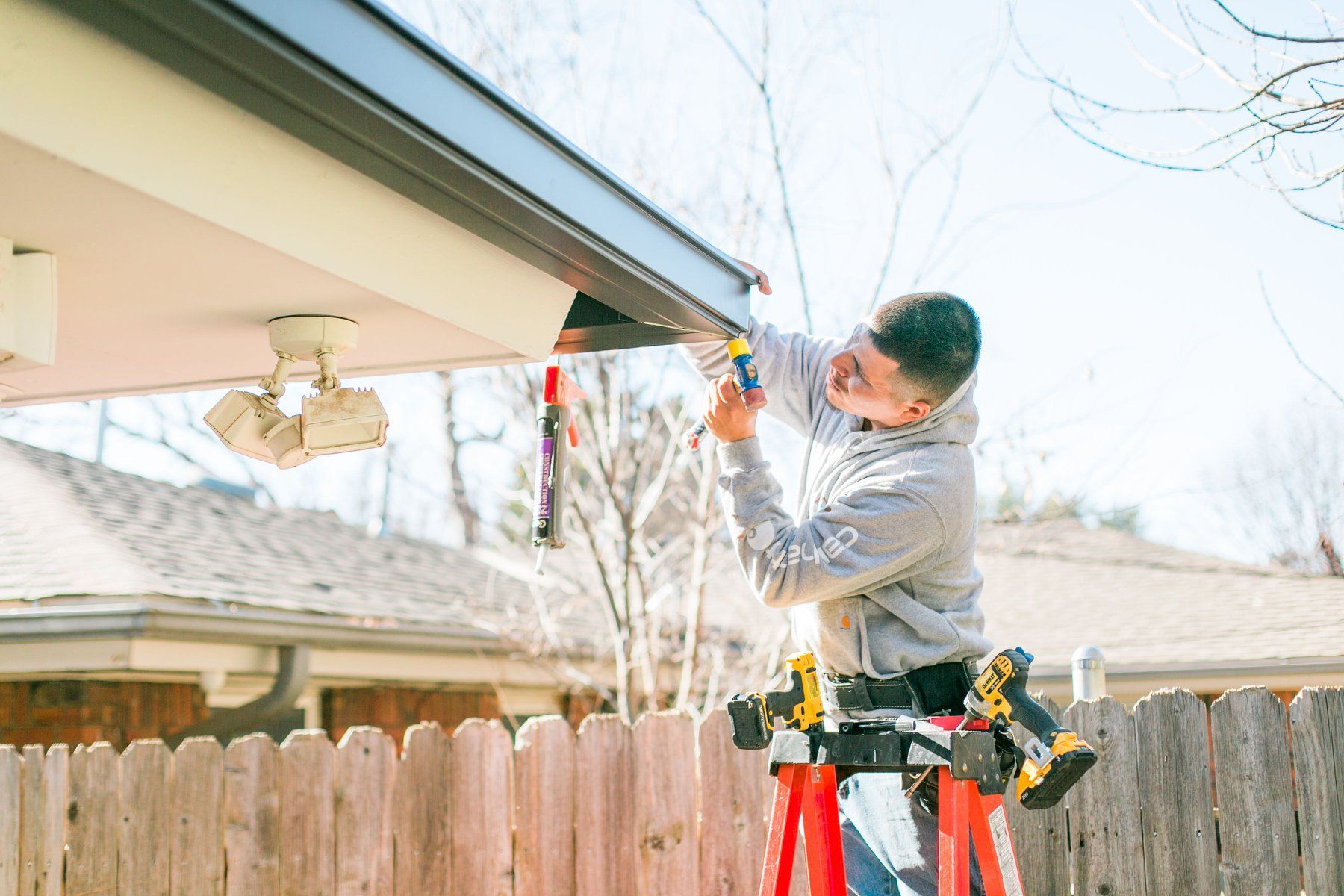 A man is standing on a ladder fixing a gutter on a house.