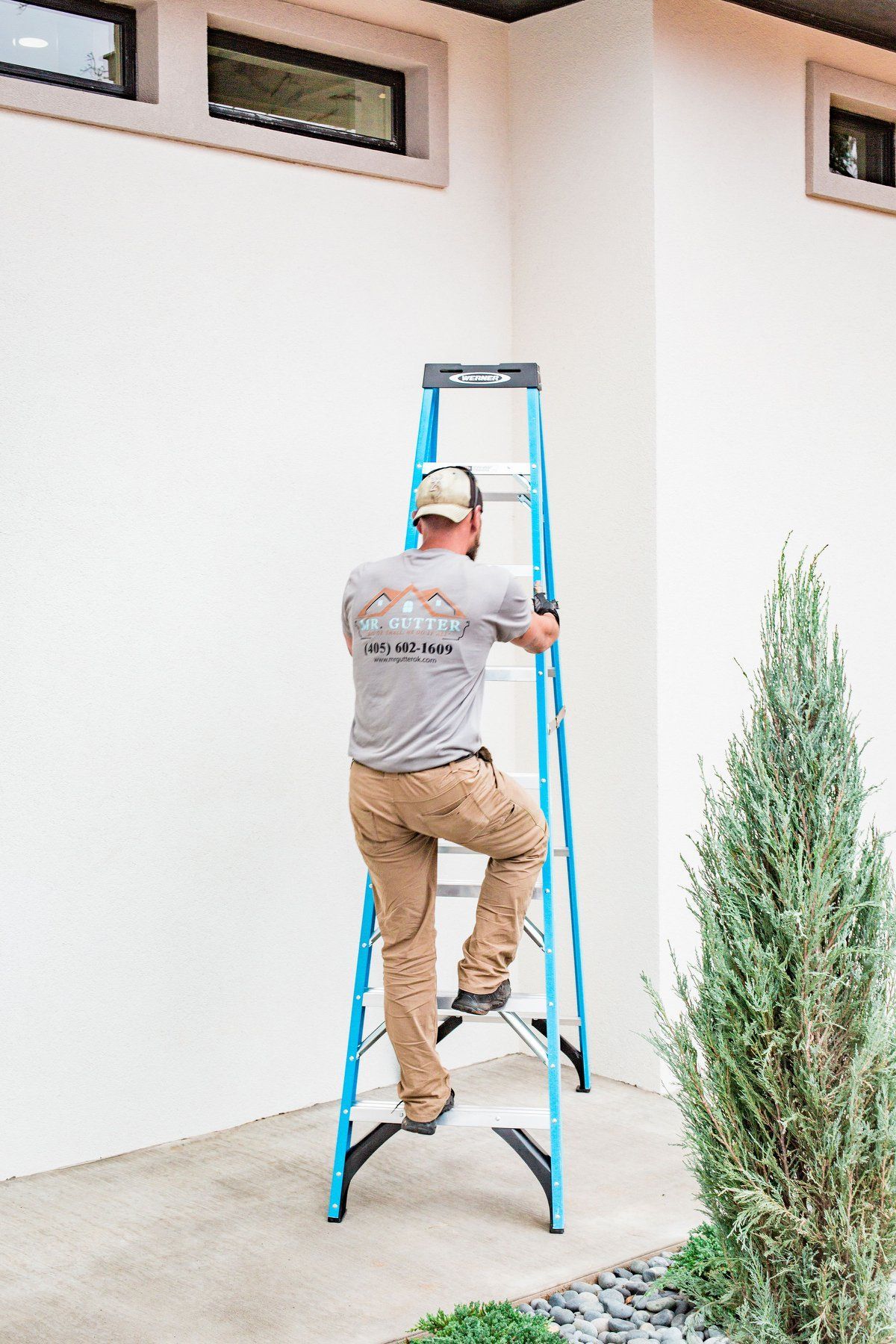 A man is climbing a blue ladder to paint a wall.