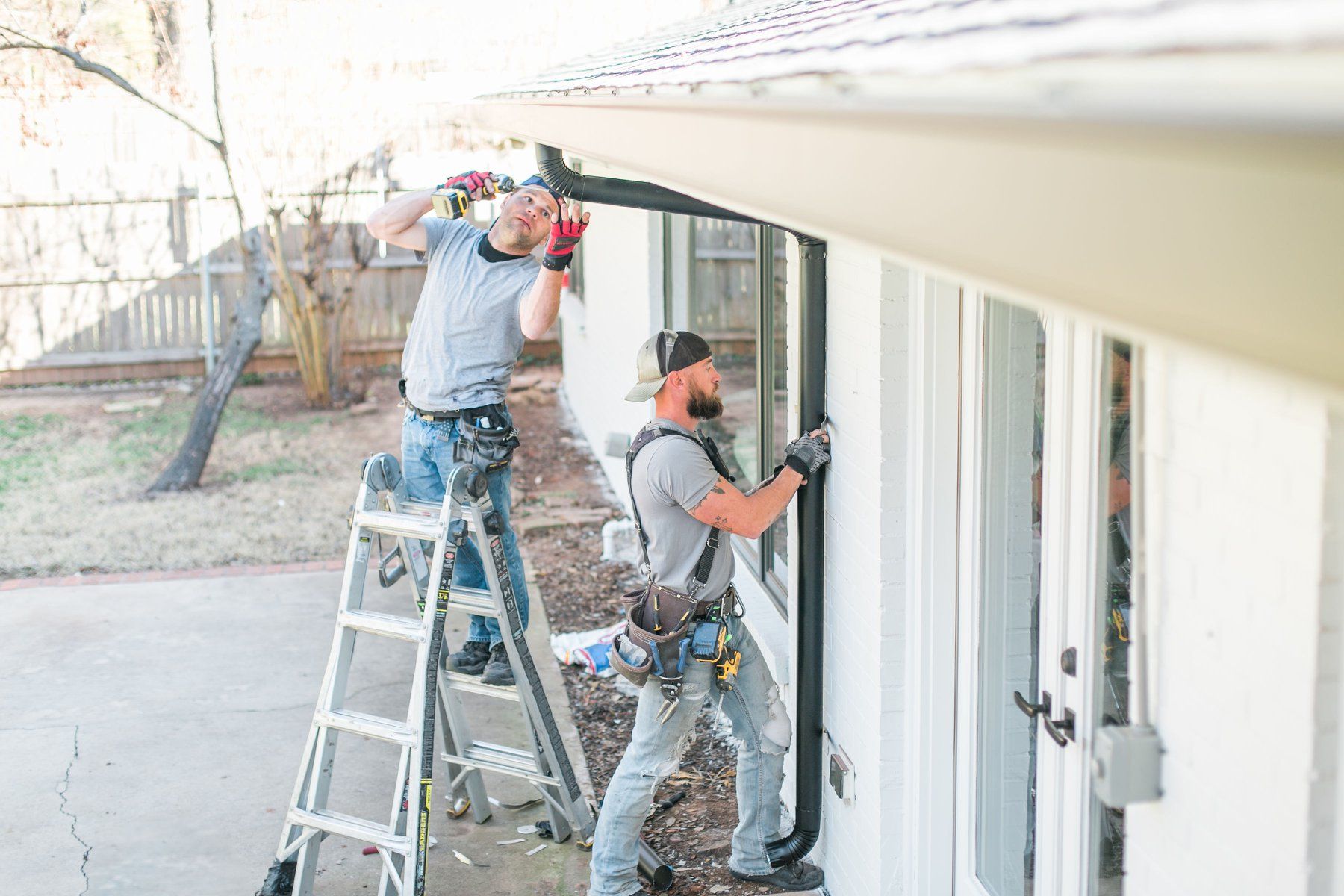 Two men are working on a gutter on the side of a house.