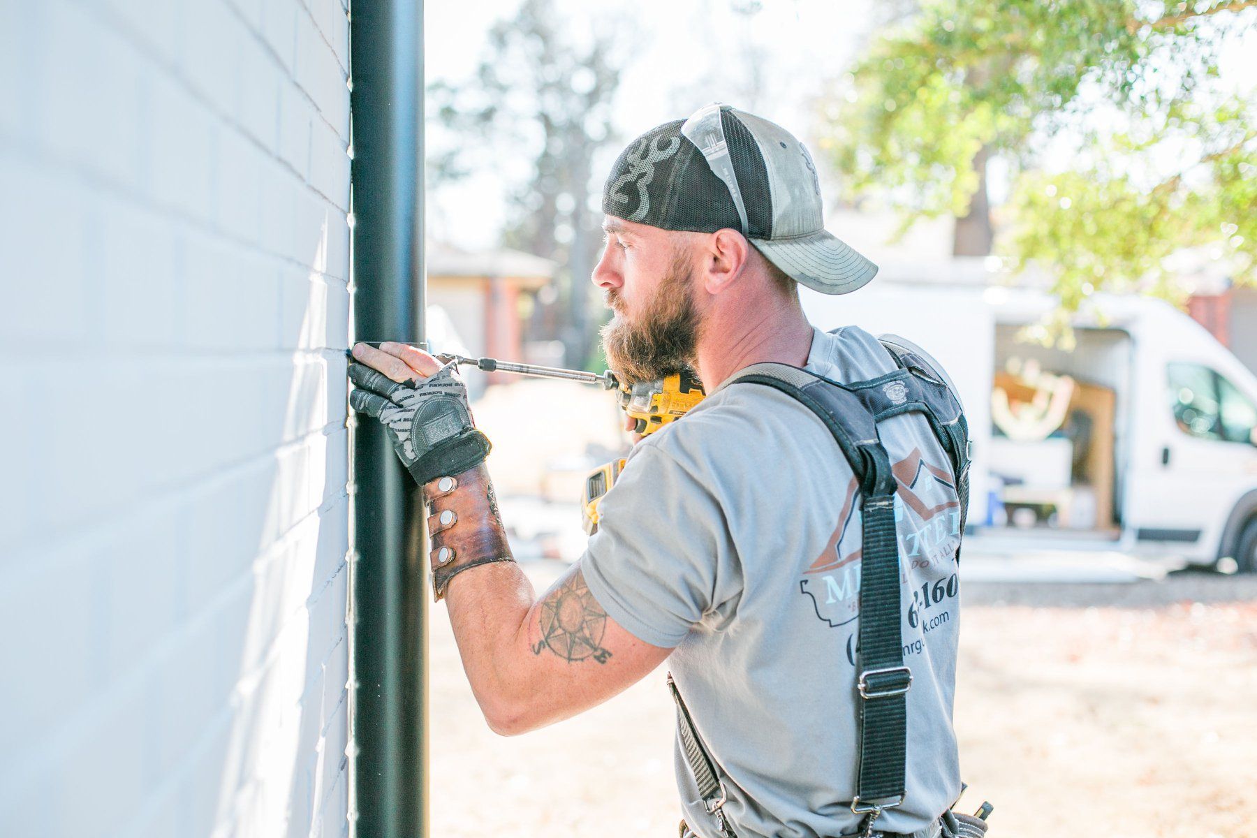 A man is using a drill to fix a pipe on a wall.