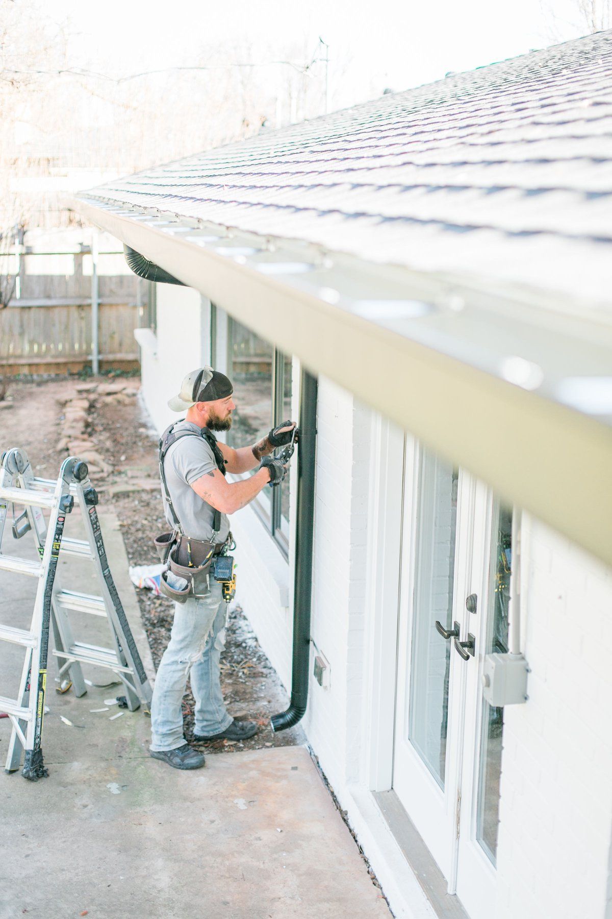 A man is installing a gutter on the side of a house.