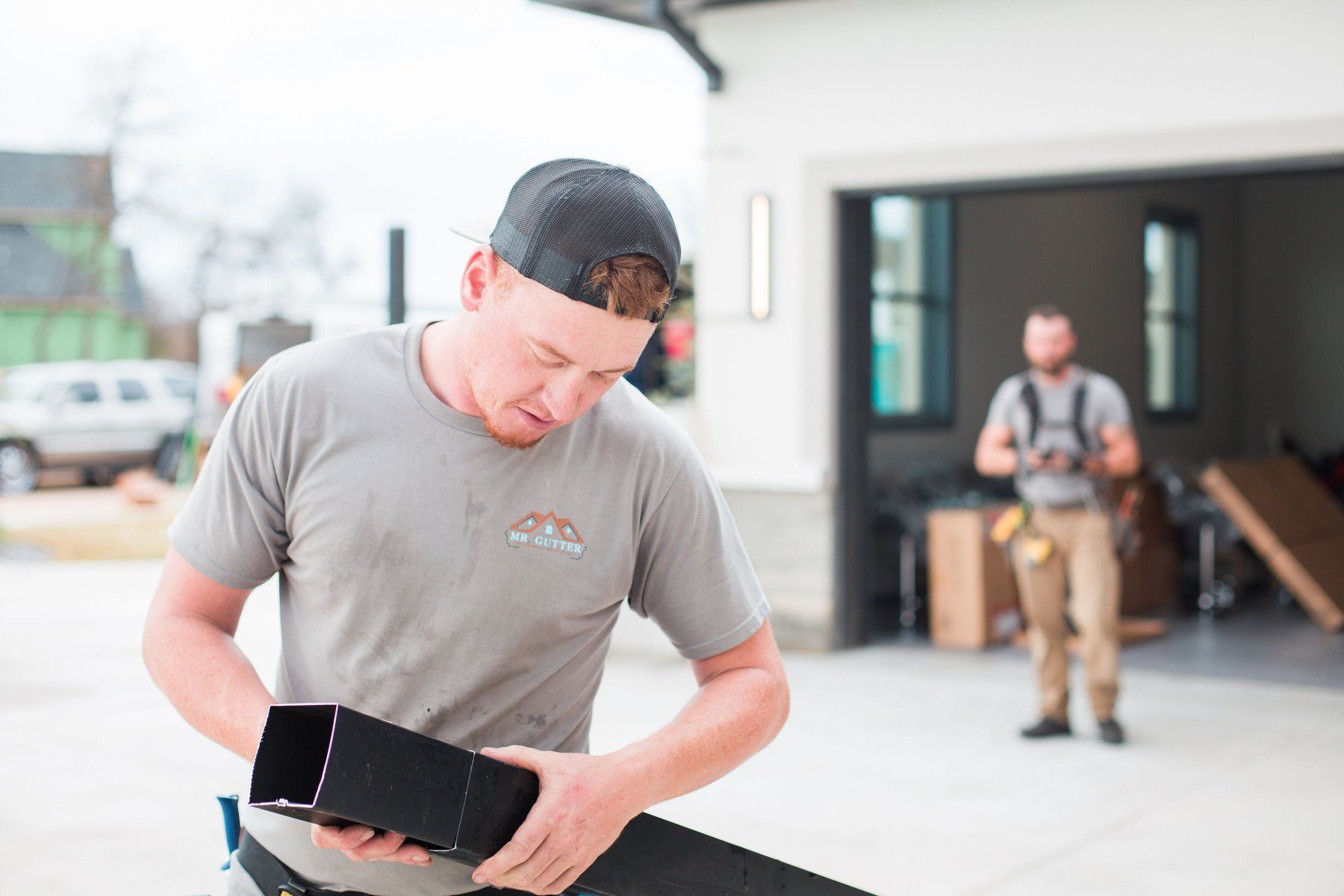 A man is standing in front of a garage holding a piece of metal.