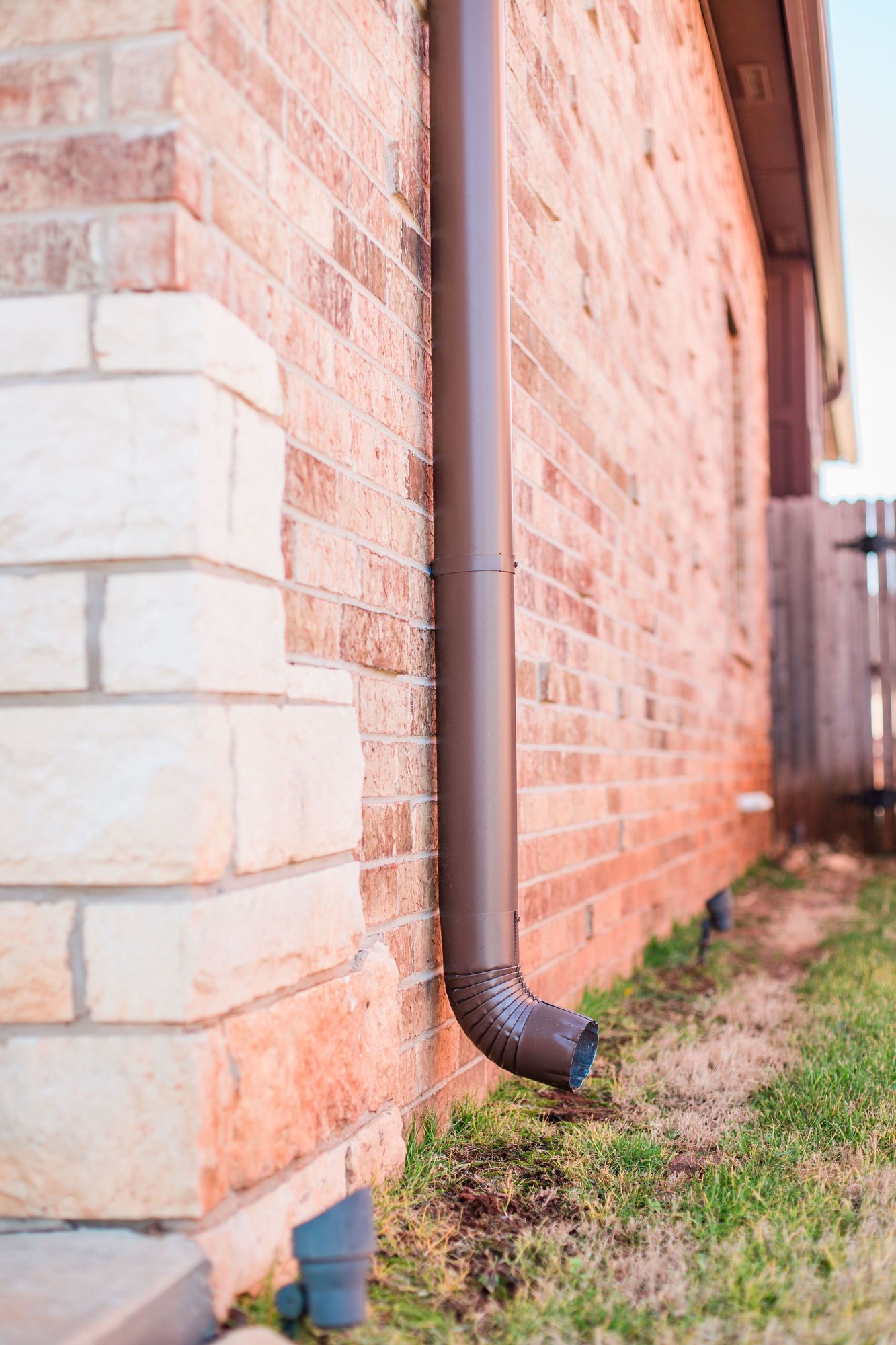 A brown gutter is attached to the side of a brick building.