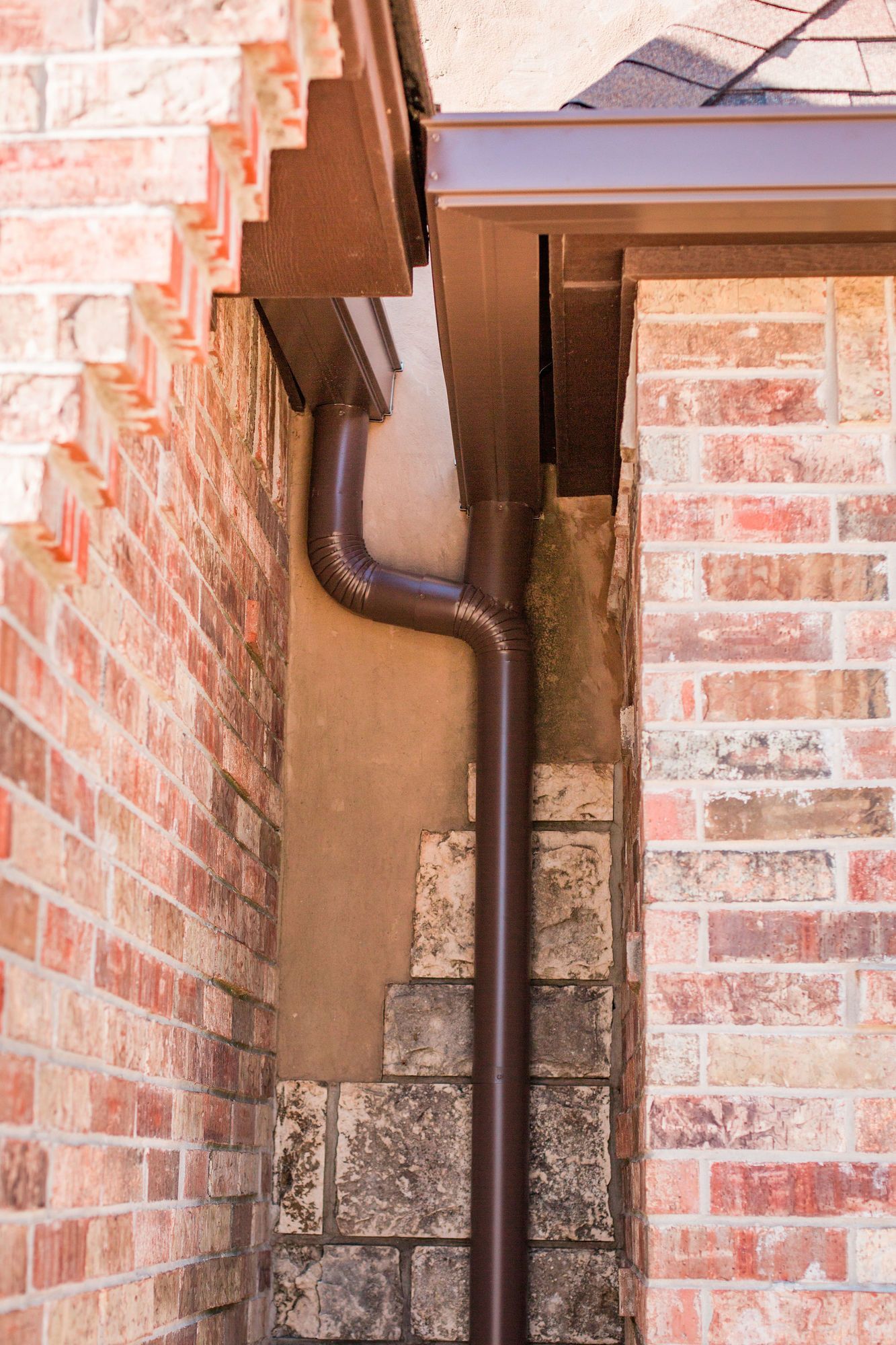 A close up of a brown gutter on a brick wall.