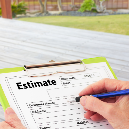 Person writing on an estimate form with a blue pen, blurred outdoor setting in the background.