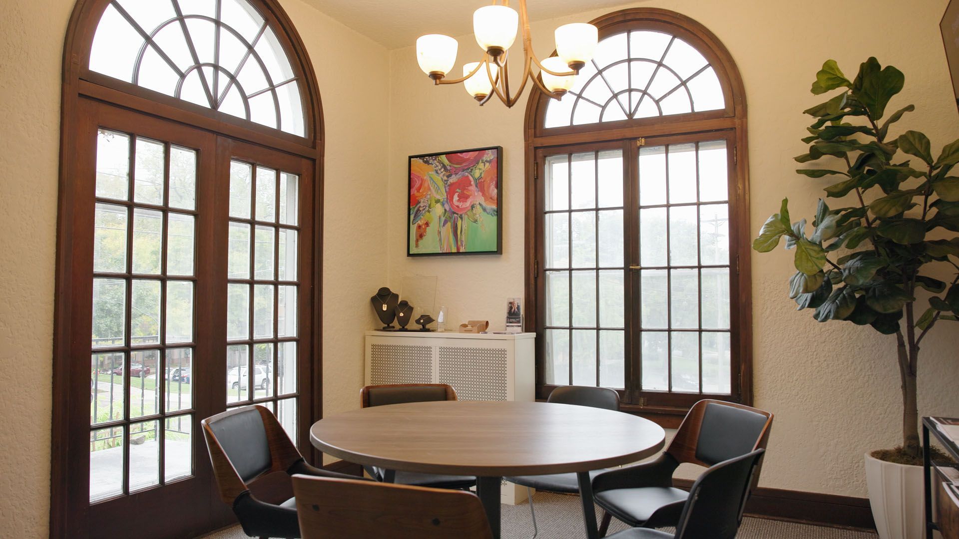 Dining room with round table, chairs, arched windows, and a large plant.