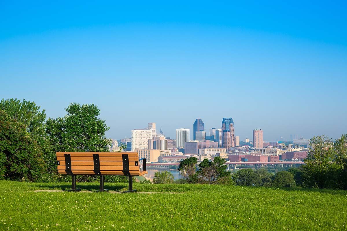 Wooden park bench overlooking a cityscape under a clear, blue sky.