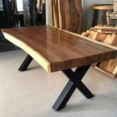 Mesa de comedor de madera con borde natural y patas de metal negro en forma de X en un entorno de taller.