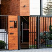 Portón de madera y metal negro con panel intercomunicador y puerta de vidrio