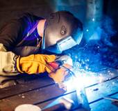 Soldador con casco, soldando metal con luz azul brillante y chispas en un taller.