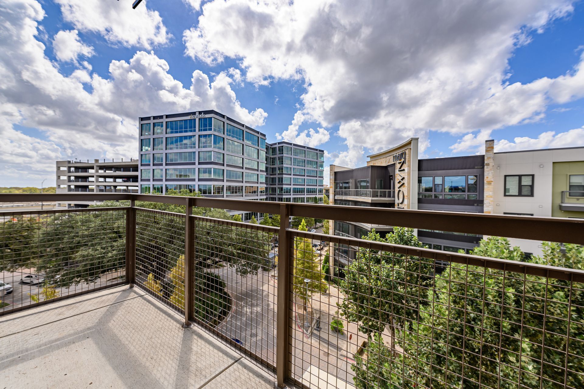 A balcony view of a sunny courtyard surrounded by modern apartment buildings under a bright, cloudy sky.