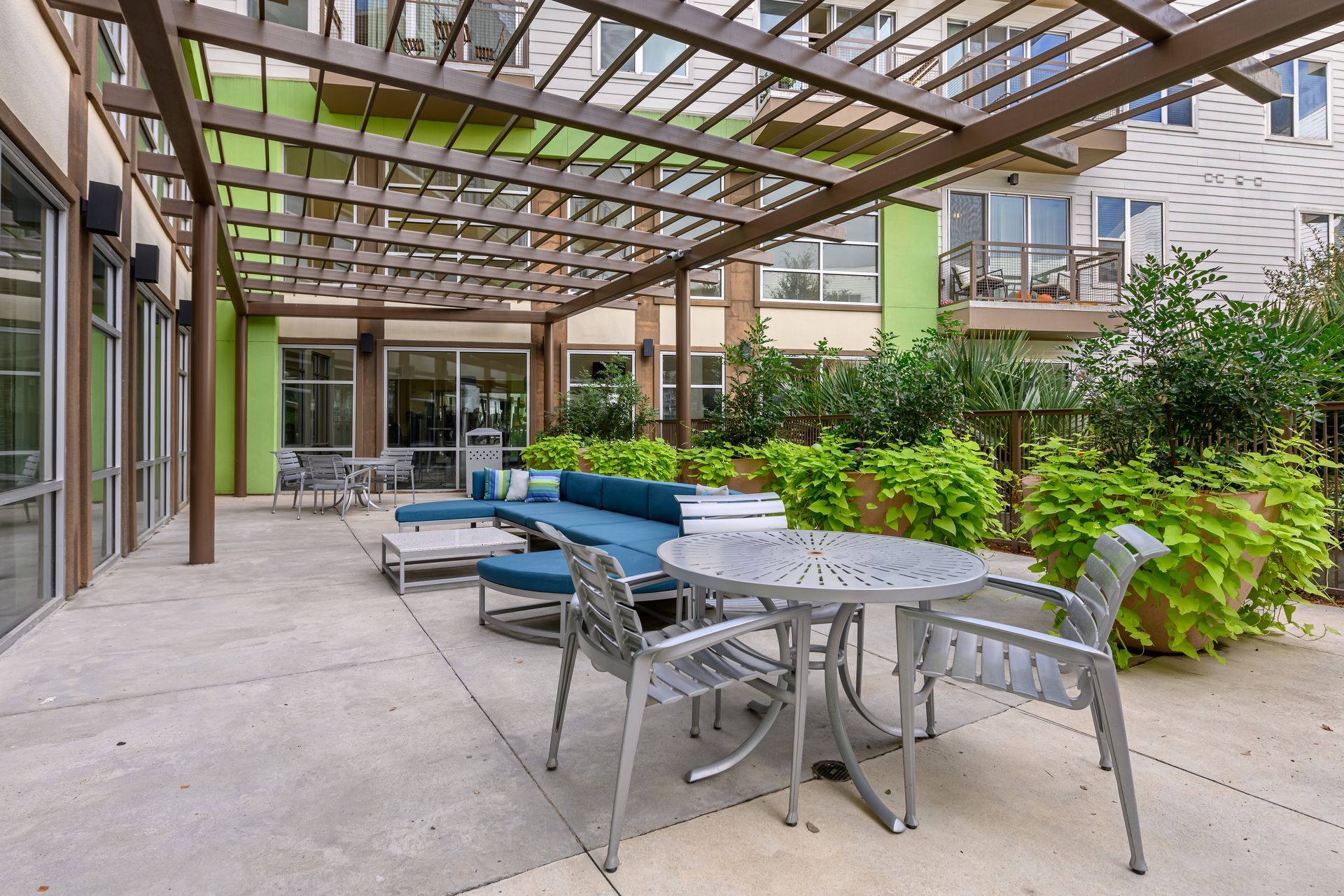 Patio area featuring a pergola, a blue sectional sofa, a round metal dining table with chairs, and potted greenery.