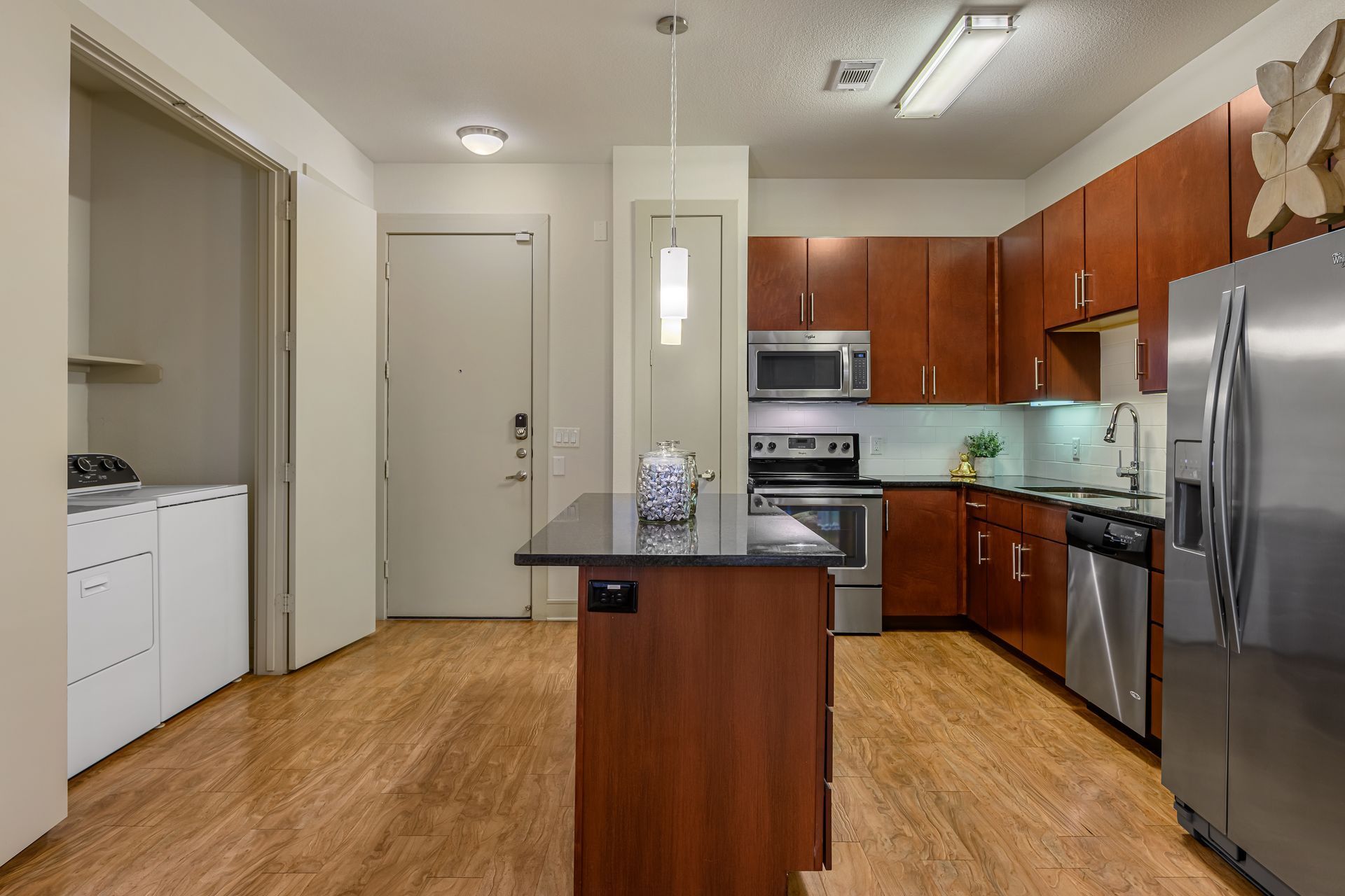 A kitchen with wood-tone cabinets, stainless steel appliances, a black-topped island, and a separate laundry closet.