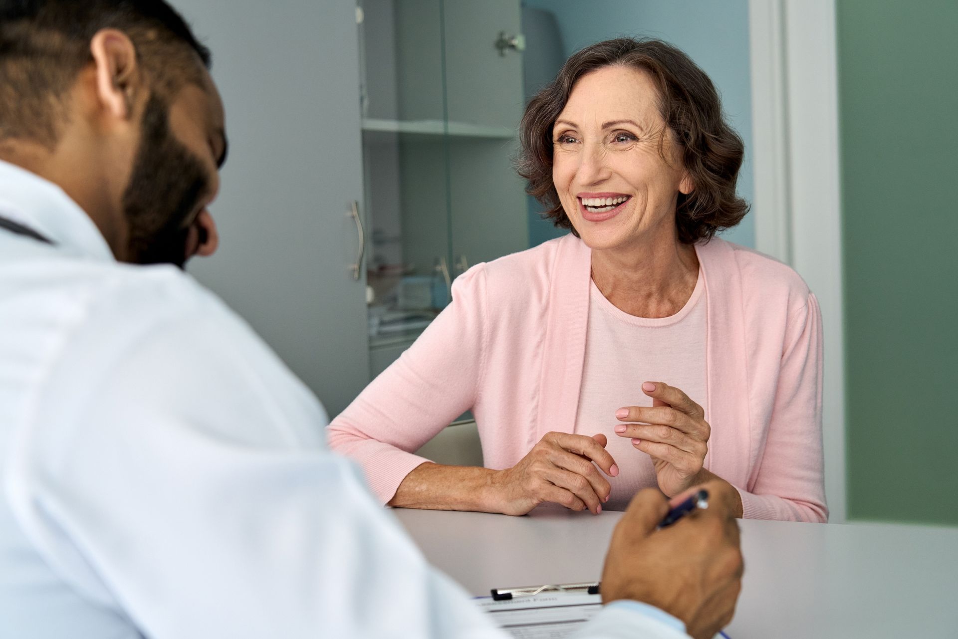 stock-photo-happy-older-mature-female-patient-talking-to-indian-male-doctor-at-appointment-healthy-smiling-2036186189-2880w