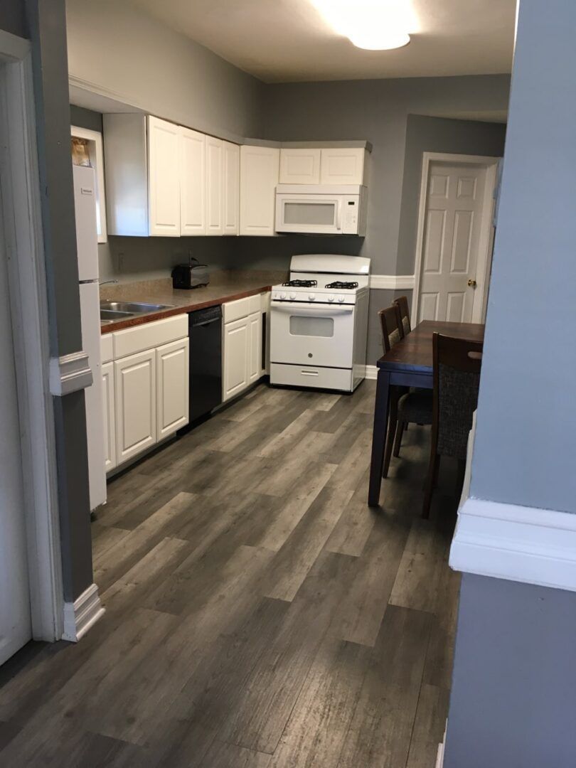 A kitchen with white cabinets , a stove , a refrigerator , a microwave and a table.