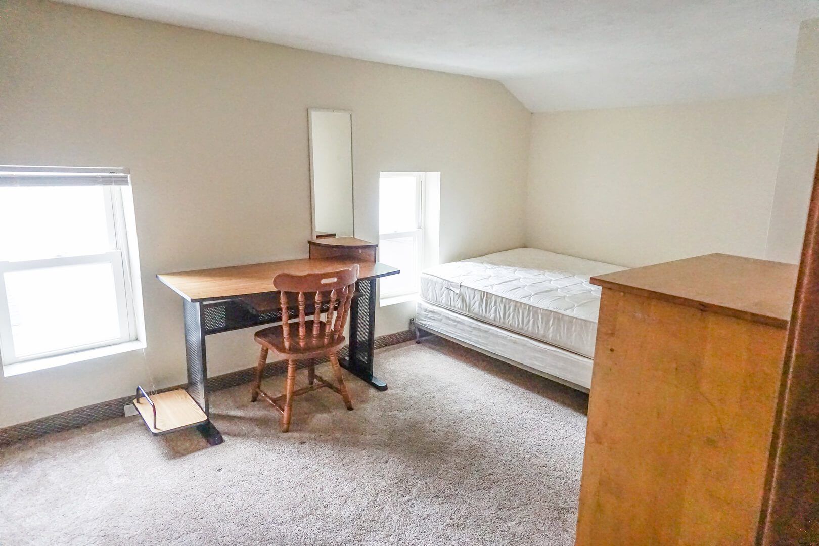 A bedroom with a bed , desk , chair and dresser.