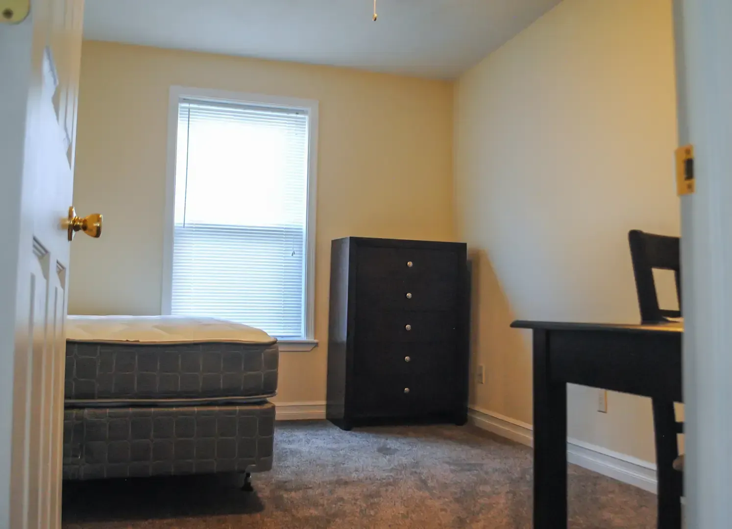 A bedroom with a bed a desk a dresser and a window