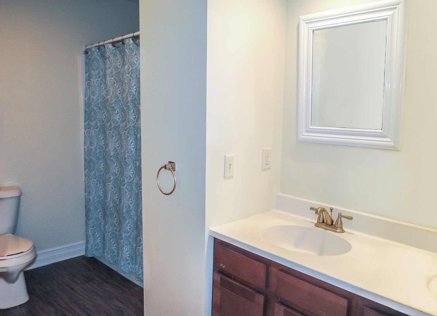 A bathroom with a toilet , sink , mirror and shower curtain.