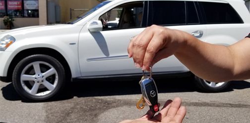 A person is holding a car key in front of a white suv.