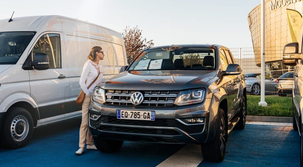 A woman is standing next to a volkswagen amarok truck in a parking lot.