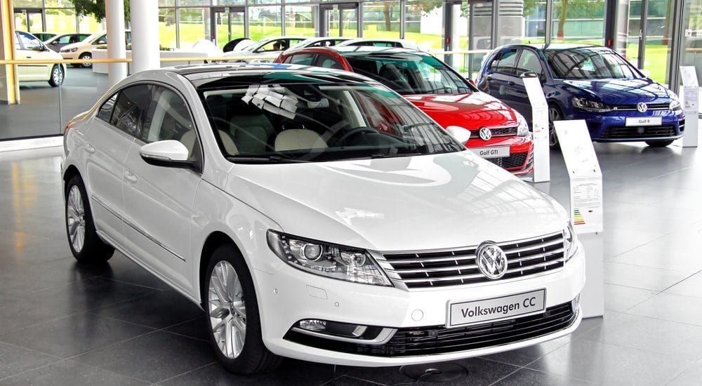 A white volkswagen cc is parked in a showroom next to other cars.