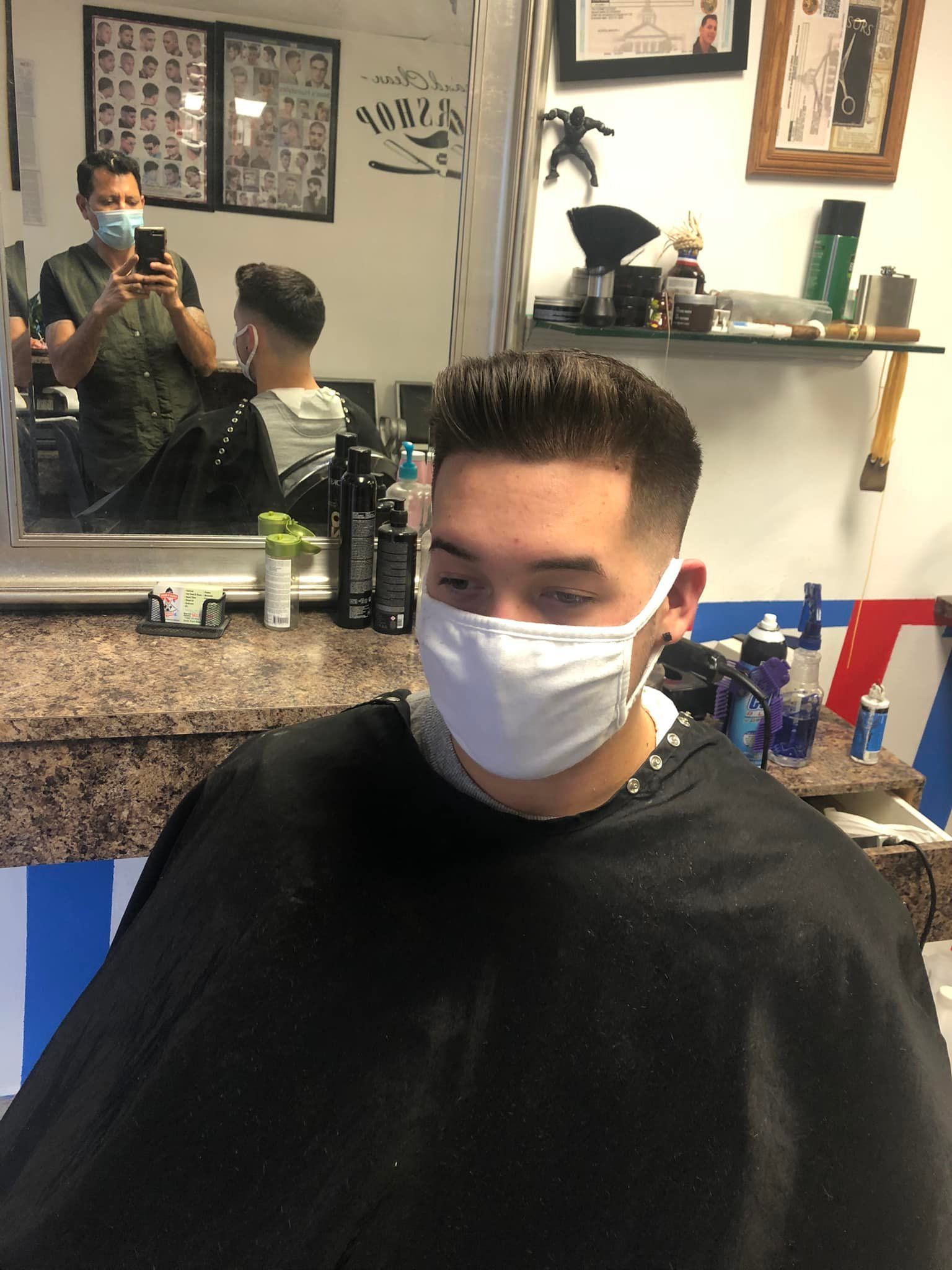 A man wearing a mask is getting his hair cut at a barber shop.