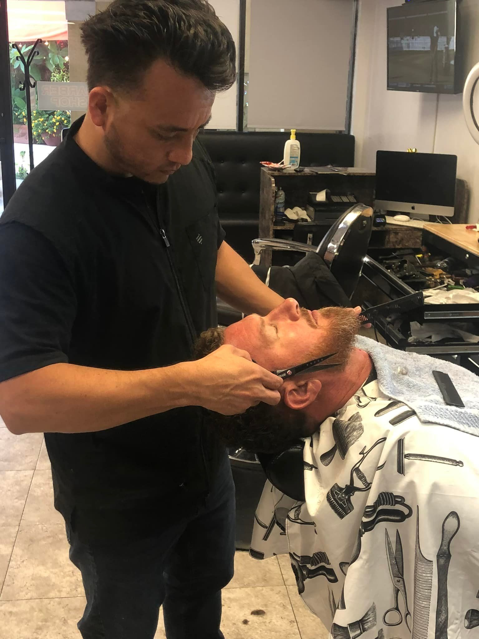A man is getting his beard shaved by a barber in a barber shop.