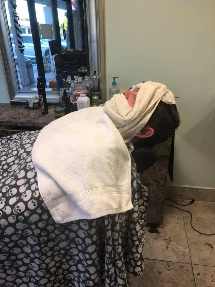 A man is getting a shave at a barber shop with a towel wrapped around his head.