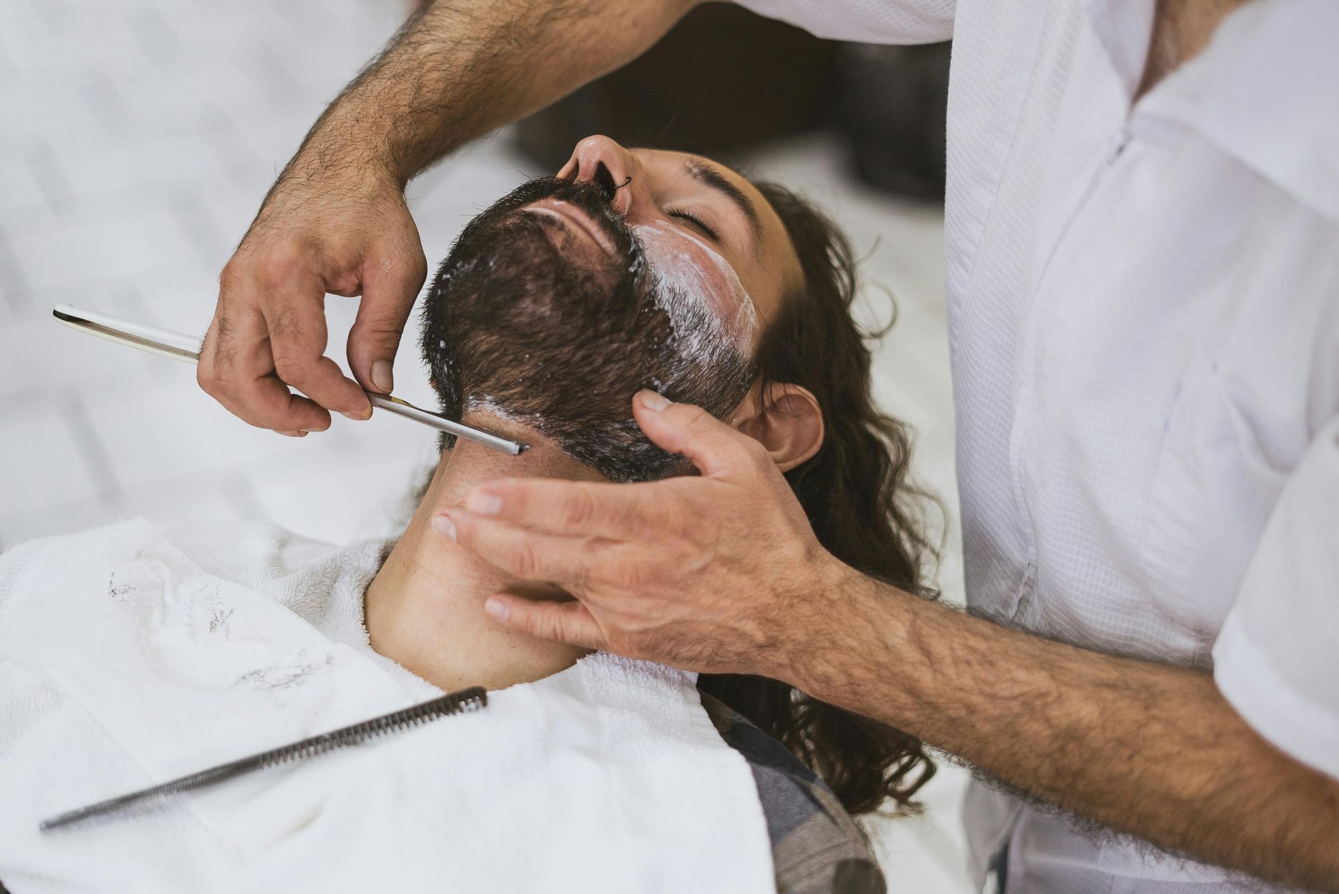 A man is getting his beard shaved by a barber.