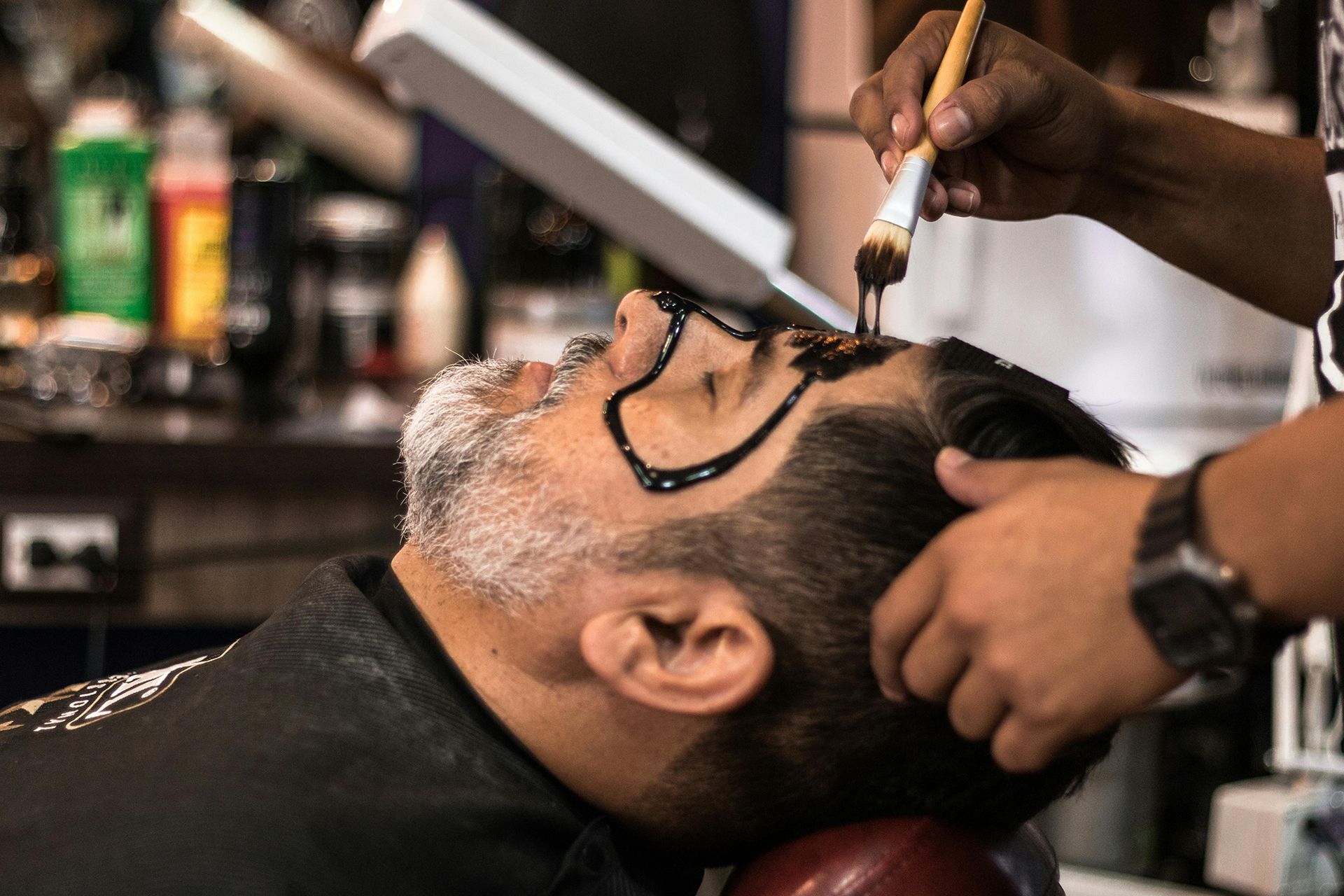 A man is getting his face painted in a barber shop.
