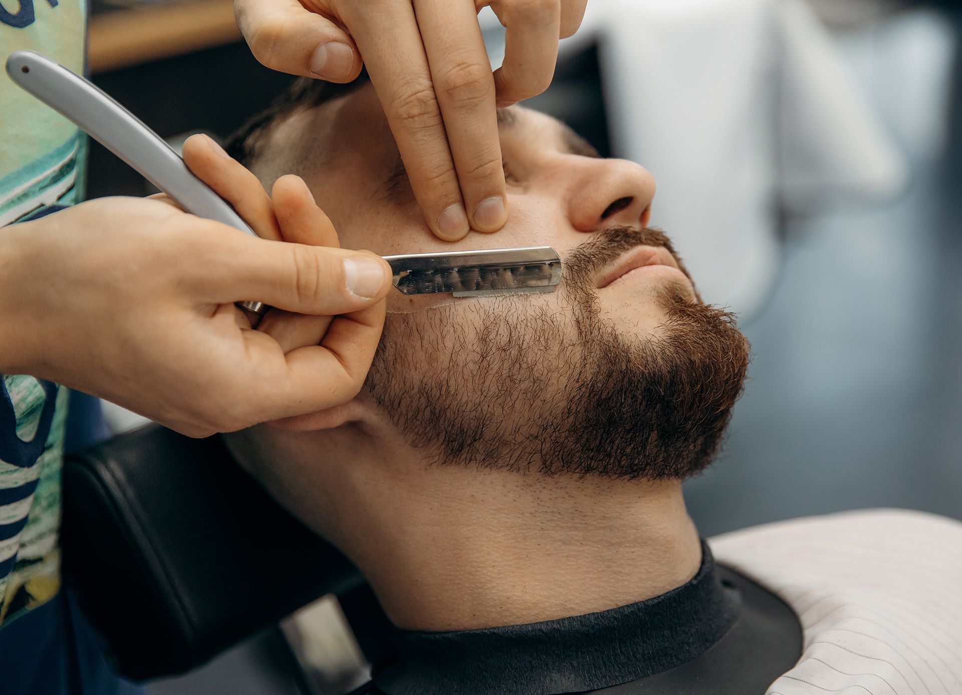 A man is getting his beard shaved by a barber with a razor.