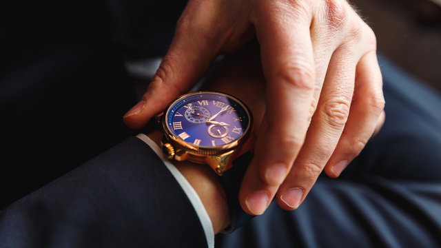 Close-up of a silver wristwatch with a black dial and gold hands on a metal mesh strap