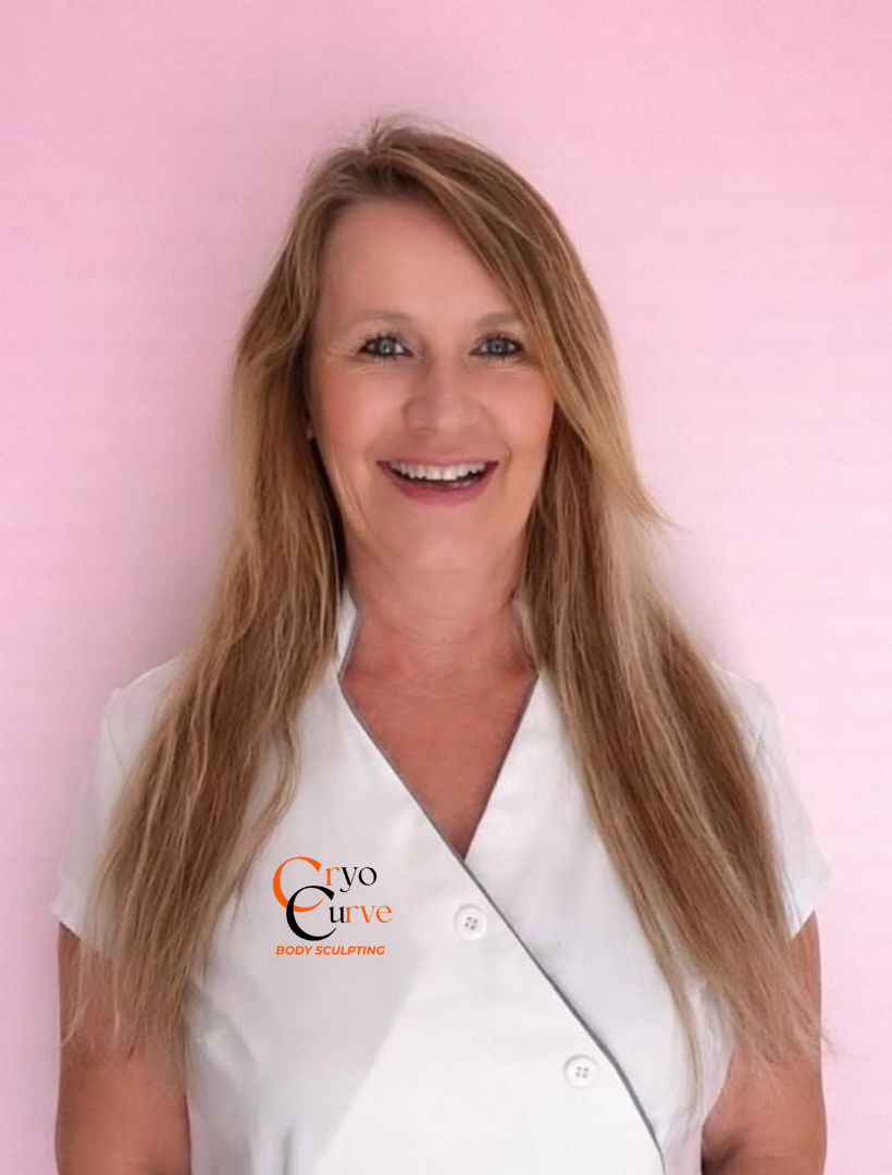 Woman in a white uniform smiling, standing against a pink wall. Logo on uniform.
