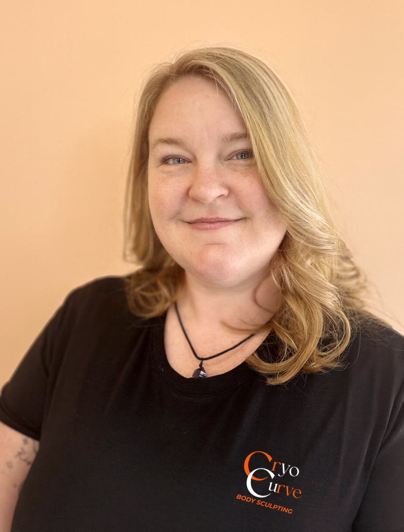 Woman with blond hair wearing a black shirt, smiling, in front of a peach wall.