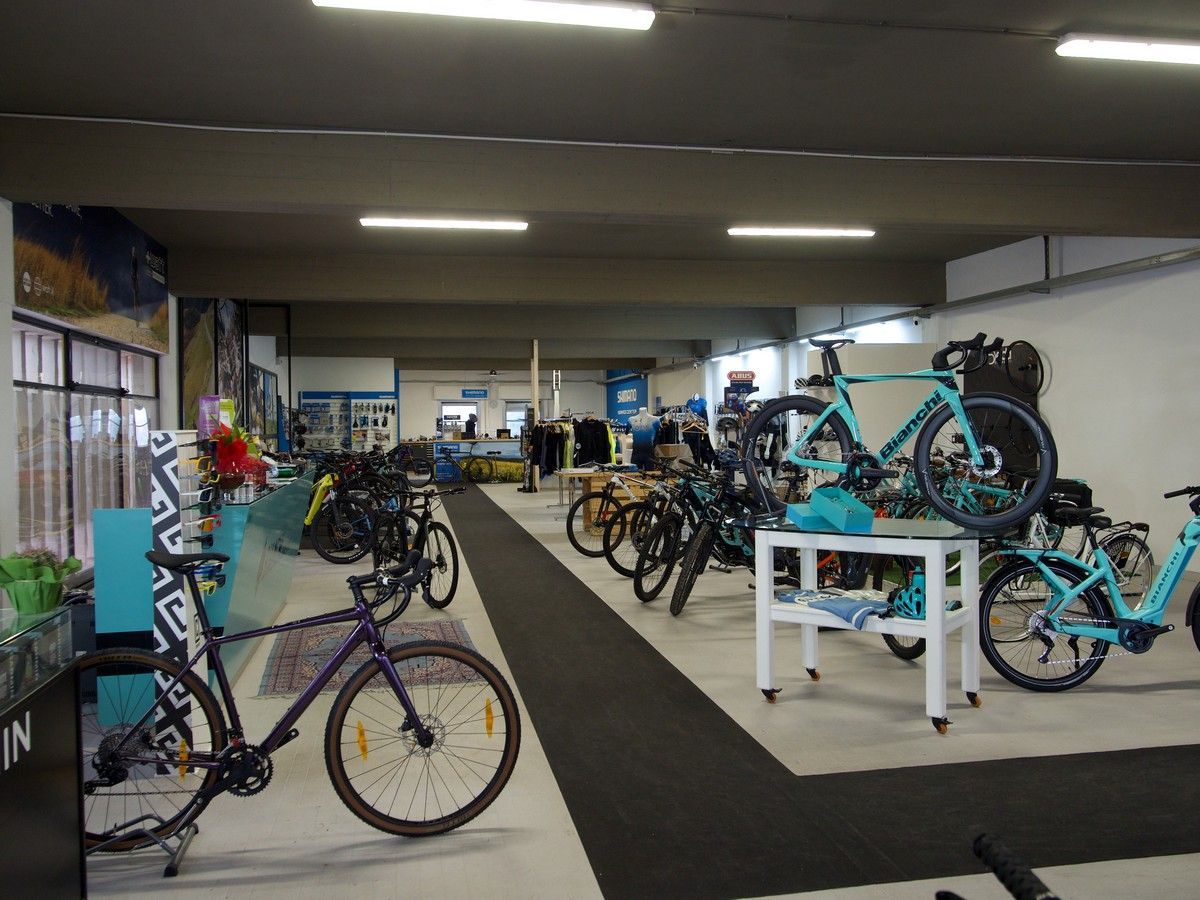 Interno di un negozio di biciclette con una bicicletta viola in primo piano, diverse altre biciclette in esposizione e un corridoio centrale.