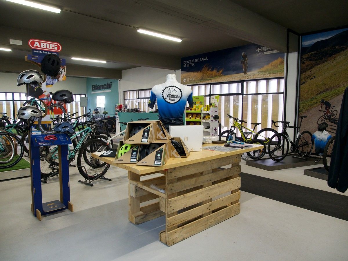 Interno di un negozio di biciclette con bancone in pallet di legno, manichino, biciclette e accessori esposti su scaffali.