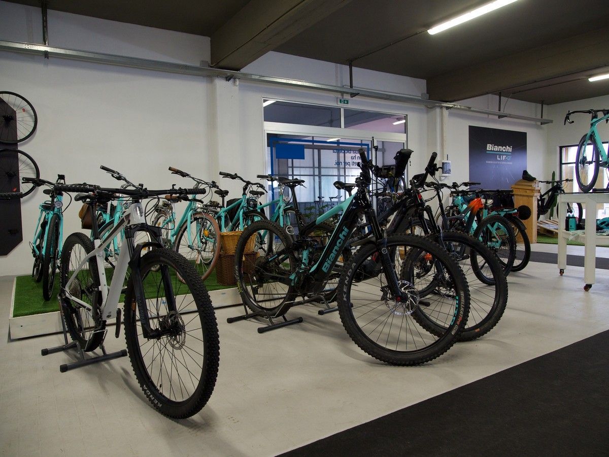 Uno spazio espositivo con diverse mountain bike color verde acqua e grigie parcheggiate su dei cavalletti.