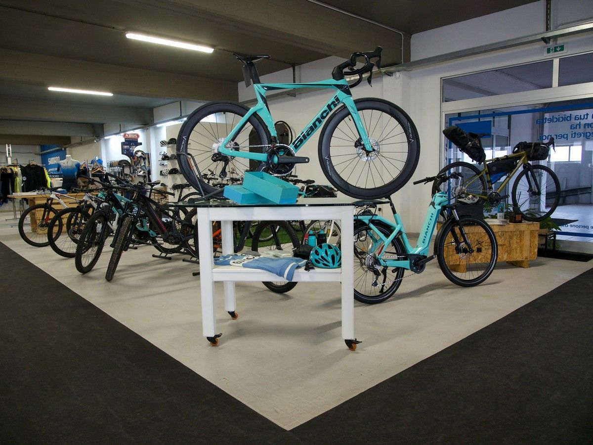 In un negozio, una vetrina espone biciclette turchesi e nere, una delle quali è posizionata su un tavolo bianco, mentre le altre sono parcheggiate nelle vicinanze.