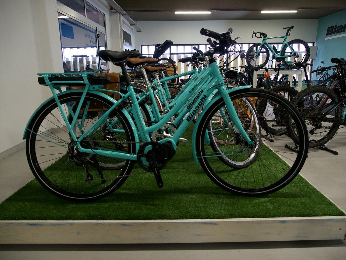 Biciclette elettriche Bianchi color turchese chiaro esposte su una piattaforma di erba sintetica all'interno di un negozio di biciclette.