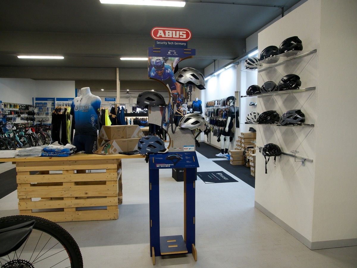 Un espositore per caschi da bicicletta a marchio Abus in un negozio di articoli sportivi, con scaffali pieni di caschi montati su una parete bianca vicina.