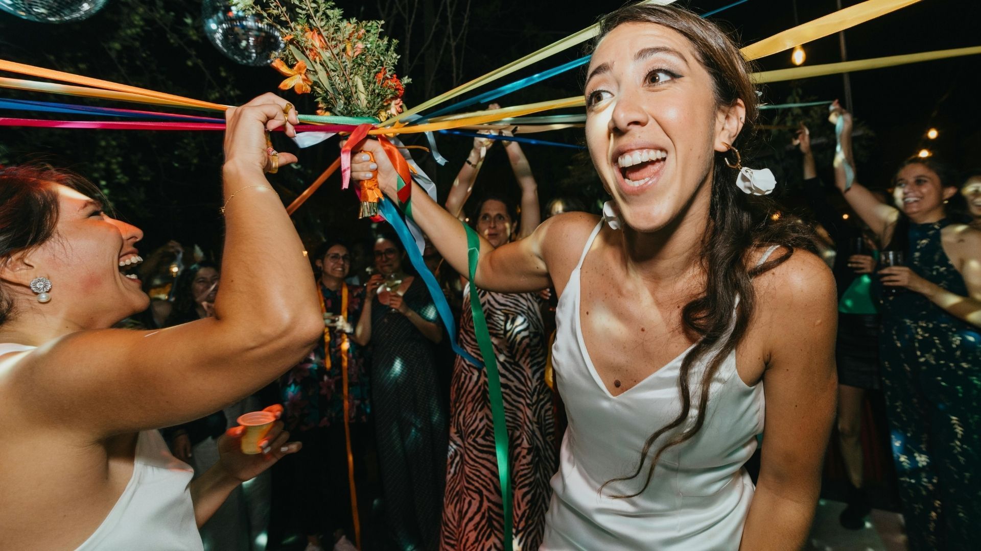Woman in white dress dances at party, holding ribbons. Others cheer in background.
