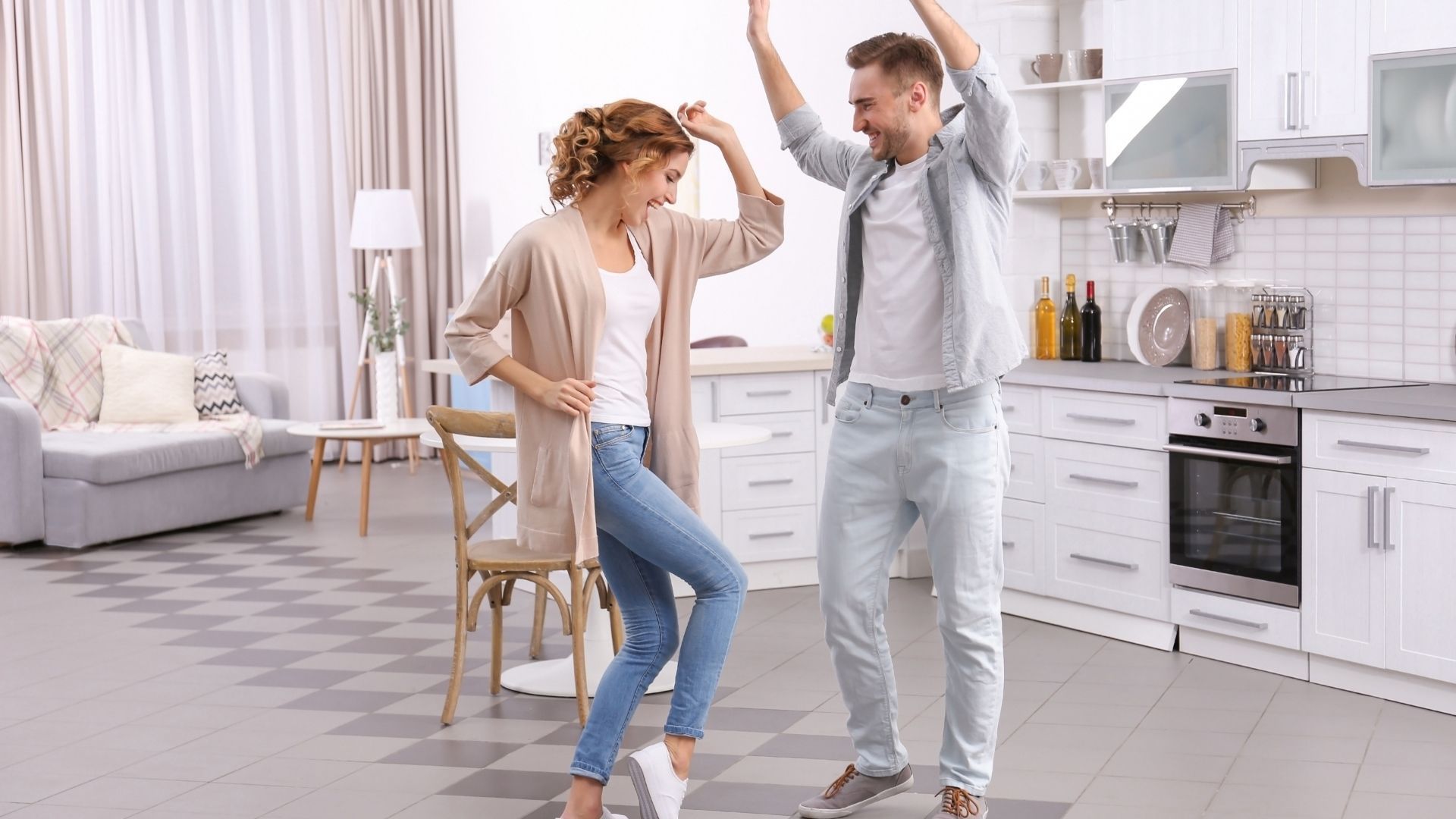 Couple dancing in their kitchen, smiling and raising their arms in celebration.